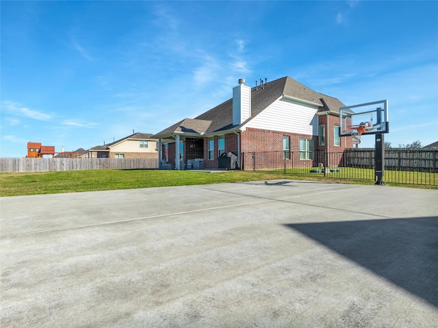 exterior space with a lawn, basketball hoop, and fence