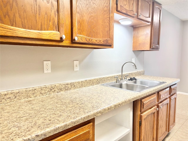 kitchen with light tile patterned floors, a sink, baseboards, light countertops, and brown cabinetry