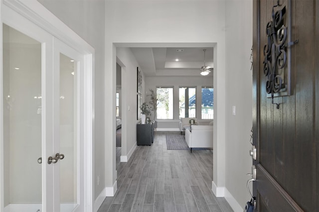 foyer with ceiling fan, baseboards, a raised ceiling, and wood finished floors