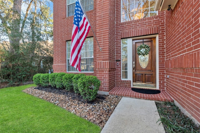 entrance to property featuring brick siding and a lawn