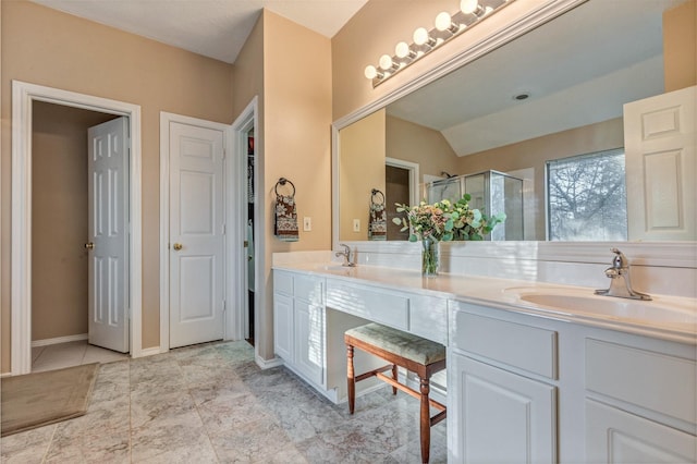 full bathroom featuring double vanity, a stall shower, a sink, and baseboards