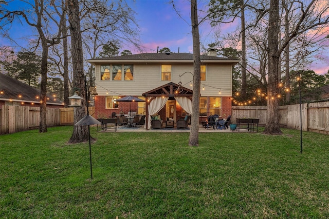 back of house at dusk featuring a yard, brick siding, a patio, and a fenced backyard