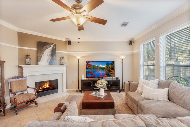 tiled living room with ceiling fan, a fireplace, visible vents, and crown molding