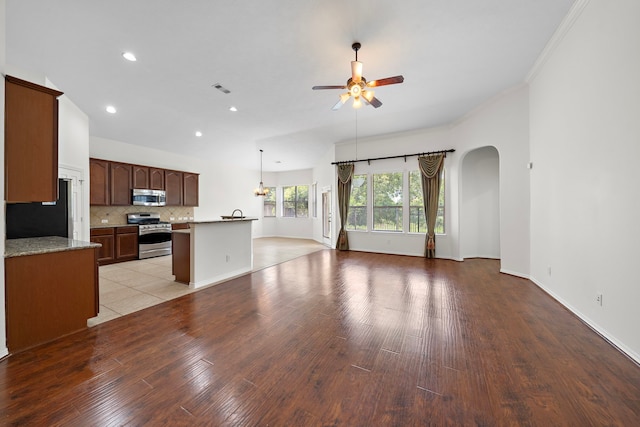 kitchen featuring ceiling fan, stainless steel appliances, light wood-style floors, open floor plan, and backsplash