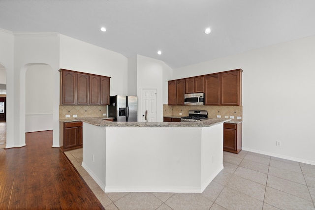 kitchen featuring arched walkways, stainless steel appliances, lofted ceiling, tasteful backsplash, and a kitchen island