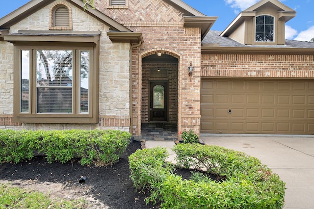 doorway to property featuring an attached garage, stone siding, driveway, and brick siding