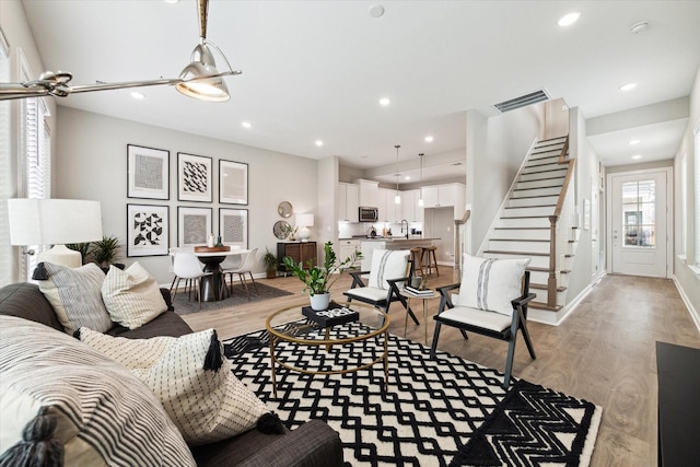 living area featuring recessed lighting, visible vents, baseboards, light wood-style floors, and stairway