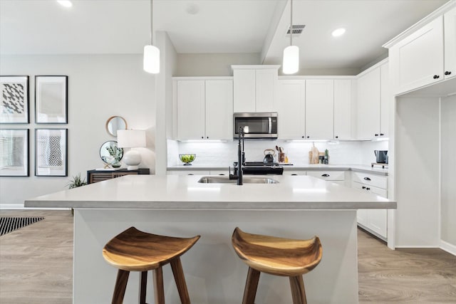 kitchen with light wood-style flooring, visible vents, stainless steel microwave, and a breakfast bar