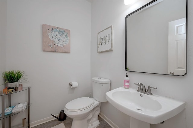 half bath with toilet, baseboards, a sink, and wood finished floors