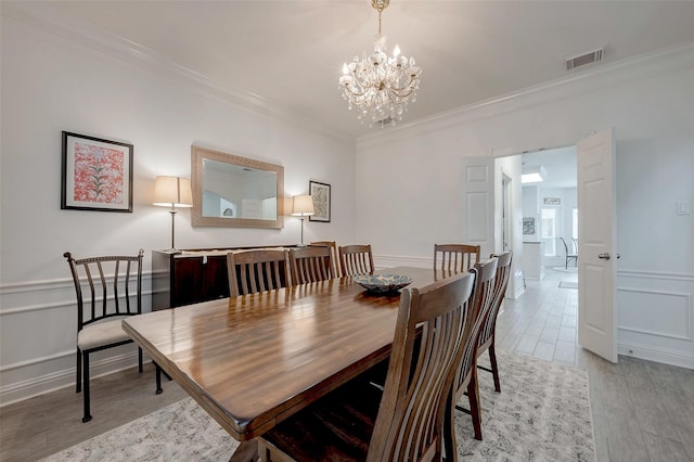 dining room with light wood-style flooring, a decorative wall, visible vents, wainscoting, and crown molding