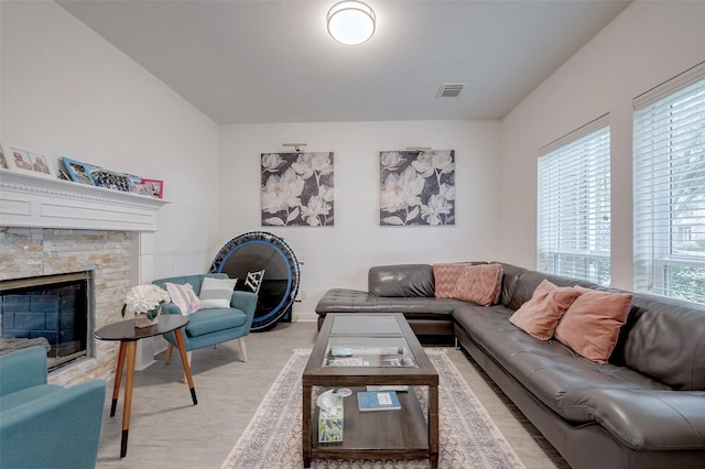 living area with light wood-style floors, visible vents, and a stone fireplace