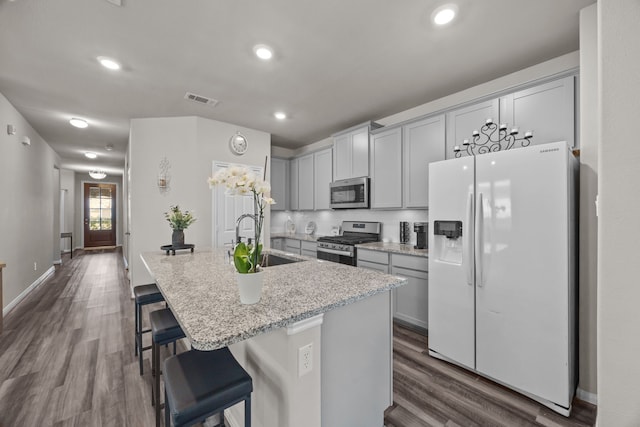 kitchen featuring stainless steel appliances, visible vents, dark wood-type flooring, a sink, and an island with sink