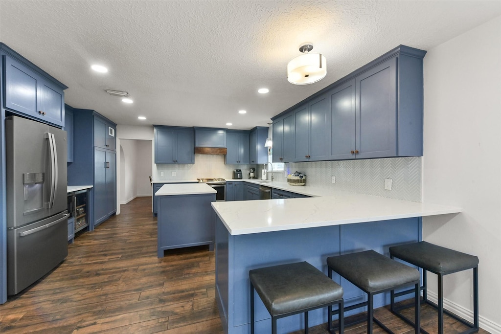 kitchen with tasteful backsplash, appliances with stainless steel finishes, dark wood-style flooring, a peninsula, and blue cabinetry