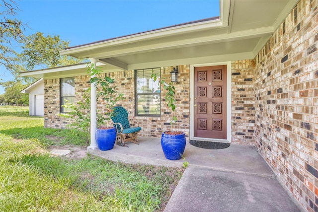 entrance to property with a porch, brick siding, and a yard