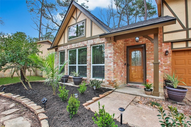 view of exterior entry with a shingled roof, brick siding, an attached garage, and stucco siding