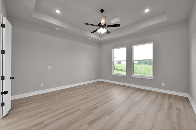 spare room featuring light wood-style floors, visible vents, a tray ceiling, and baseboards