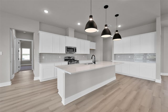 kitchen featuring stainless steel appliances, a sink, light countertops, light wood finished floors, and a large island with sink