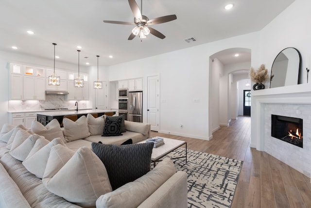 living room with a warm lit fireplace, visible vents, baseboards, light wood-style floors, and recessed lighting