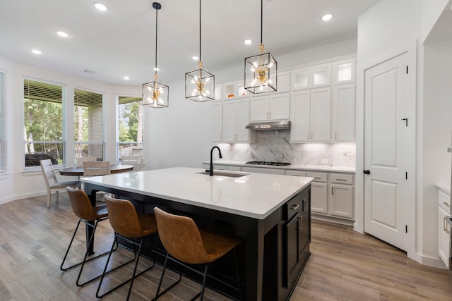 kitchen featuring a center island with sink, a sink, under cabinet range hood, gas stovetop, and backsplash