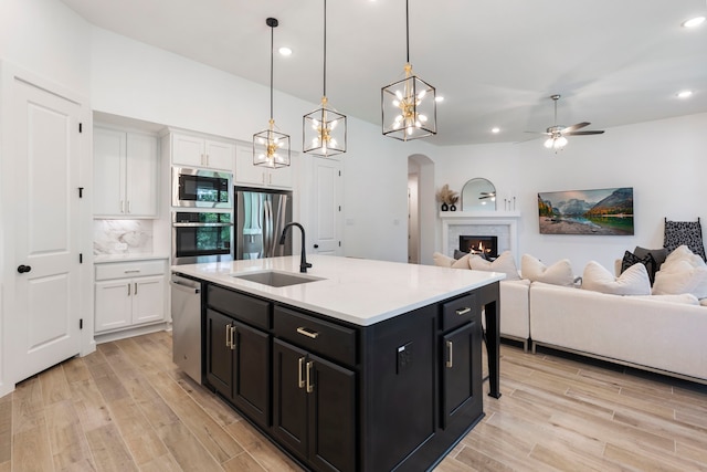 kitchen featuring stainless steel appliances, light wood-style flooring, white cabinets, a sink, and dark cabinets