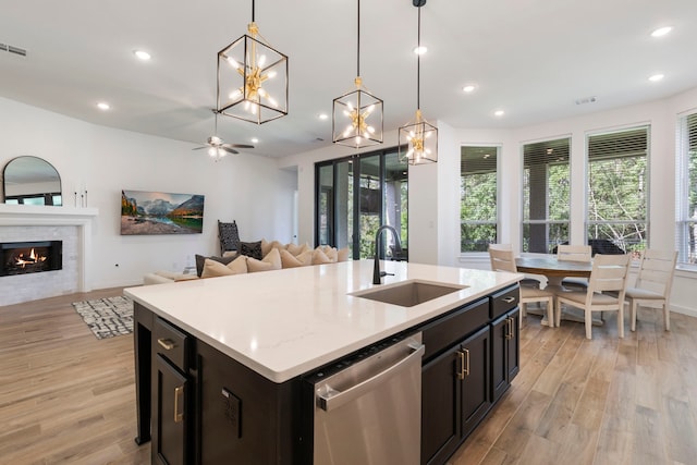 kitchen with dishwasher, a warm lit fireplace, a sink, and light wood-style flooring