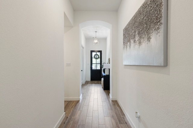 corridor featuring baseboards, arched walkways, and wood finished floors