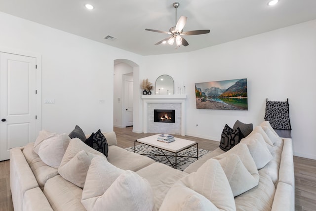 living room with arched walkways, light wood-style flooring, a tiled fireplace, and visible vents