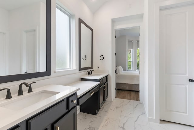 ensuite bathroom with vaulted ceiling, marble finish floor, a sink, and double vanity