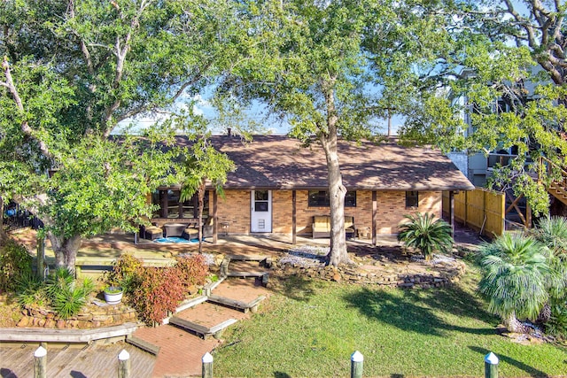 view of front of home with a front yard, a patio area, brick siding, and roof with shingles