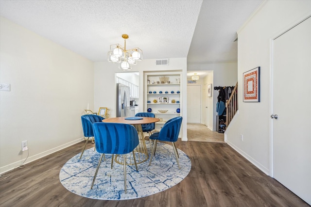 dining room featuring visible vents, wood finished floors, an inviting chandelier, a textured ceiling, and built in shelves