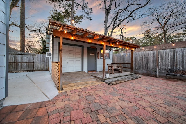 patio terrace at dusk featuring a garage and fence