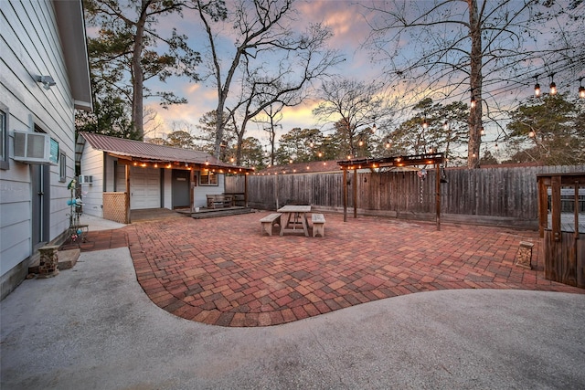 patio terrace at dusk featuring a fenced backyard, a wall unit AC, and an outdoor structure