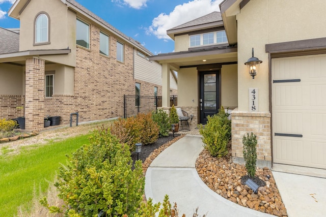 doorway to property featuring a garage, stucco siding, fence, a porch, and brick siding