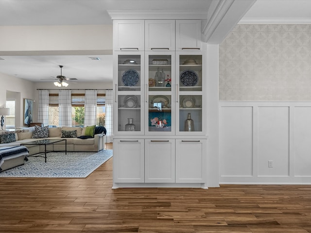 interior space with a decorative wall, wood finished floors, visible vents, a ceiling fan, and wainscoting