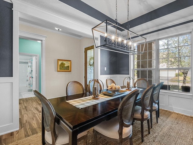 dining room featuring a notable chandelier, a decorative wall, wood finished floors, wainscoting, and crown molding