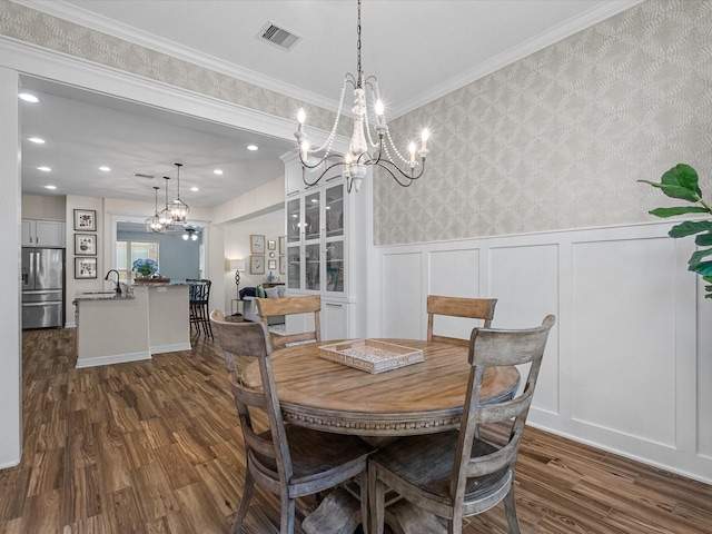 dining area with dark wood-style floors, a wainscoted wall, a notable chandelier, visible vents, and wallpapered walls