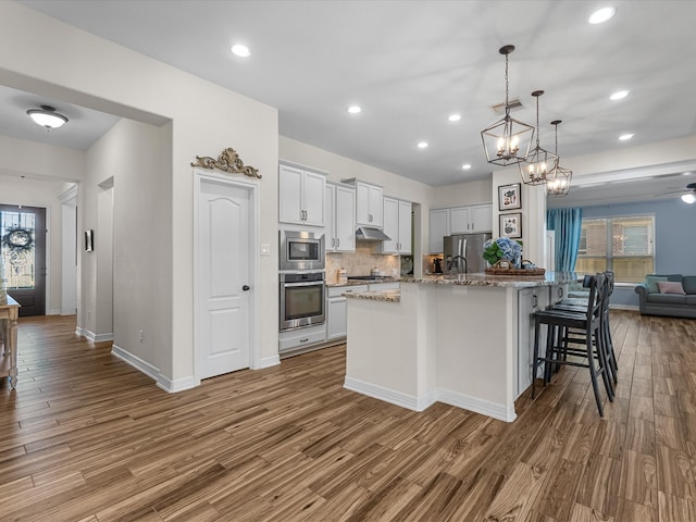 kitchen with visible vents, open floor plan, wood finished floors, stainless steel appliances, and under cabinet range hood