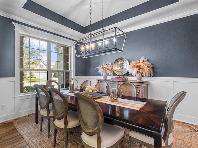 dining space with a tray ceiling, ornamental molding, wood finished floors, and wainscoting