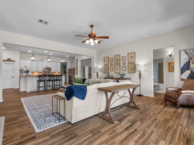 living area featuring dark wood-style floors, ceiling fan, visible vents, and baseboards