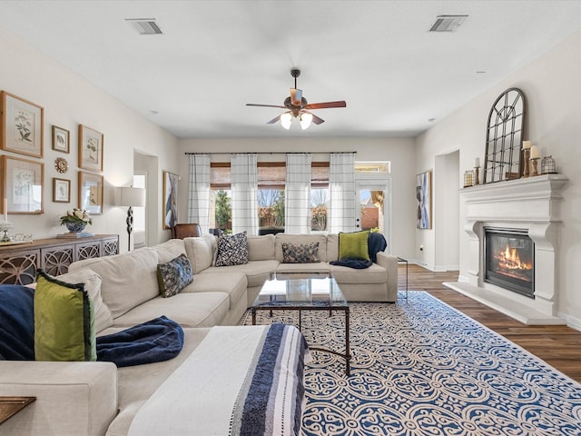 living room with wood finished floors, a glass covered fireplace, visible vents, and baseboards