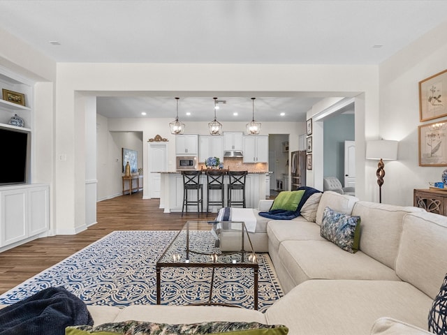 living room with dark wood-type flooring, recessed lighting, built in shelves, and baseboards