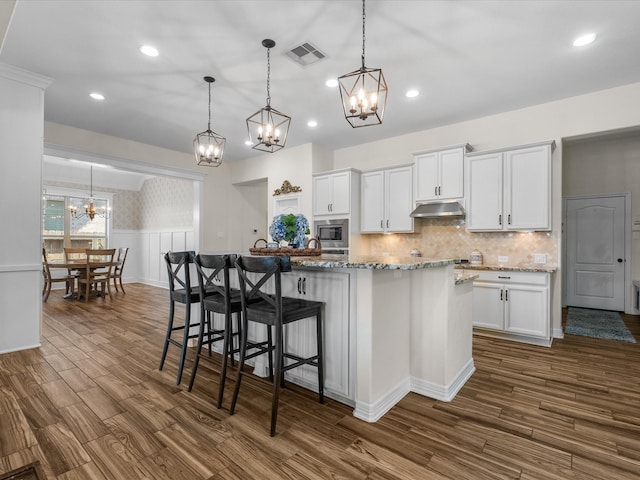 kitchen with dark wood finished floors, visible vents, stainless steel microwave, and under cabinet range hood