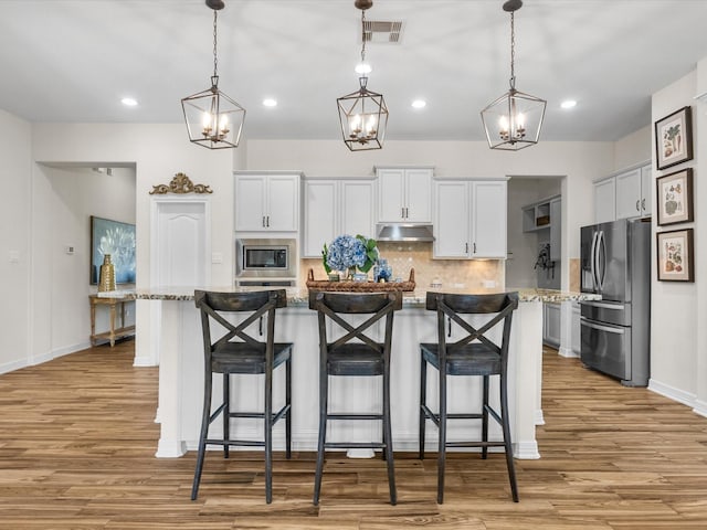 kitchen with appliances with stainless steel finishes, light wood-style floors, visible vents, and under cabinet range hood