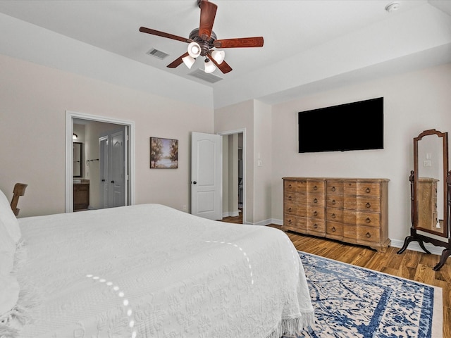 bedroom with baseboards, visible vents, ensuite bath, ceiling fan, and wood finished floors