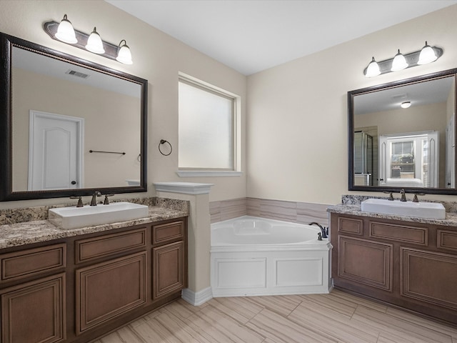 bathroom with a garden tub, two vanities, a sink, and visible vents