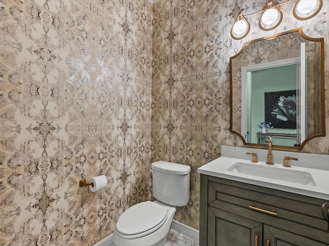 half bathroom featuring baseboards, vanity, toilet, and wallpapered walls