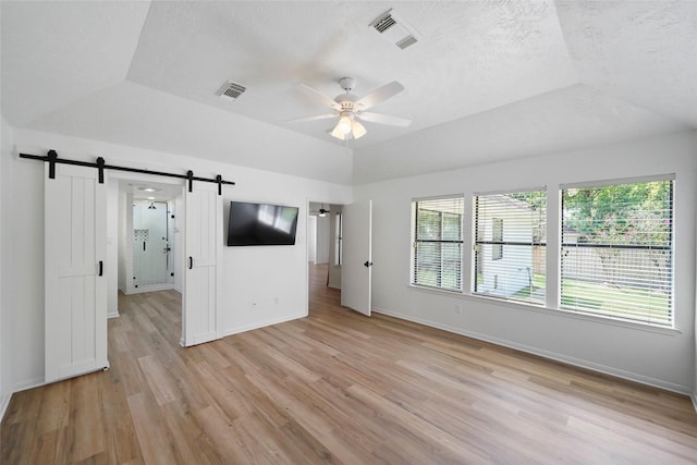 spare room featuring a textured ceiling, a barn door, light wood-type flooring, and visible vents