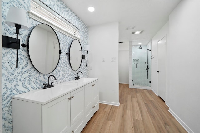 full bath featuring double vanity, a stall shower, baseboards, wood finished floors, and a sink