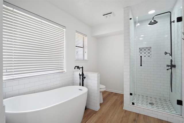 bathroom with a soaking tub, a shower stall, visible vents, and wood finished floors