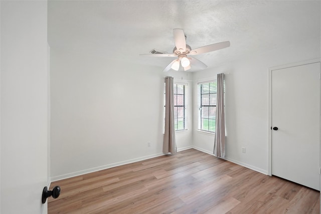 spare room with a textured ceiling, a ceiling fan, light wood-style flooring, and baseboards